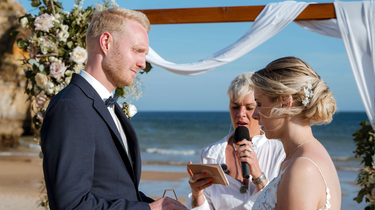 Brautpaar bei freier Trauung am Strand der Algarve mit Traurednerin vor Blumenbogen